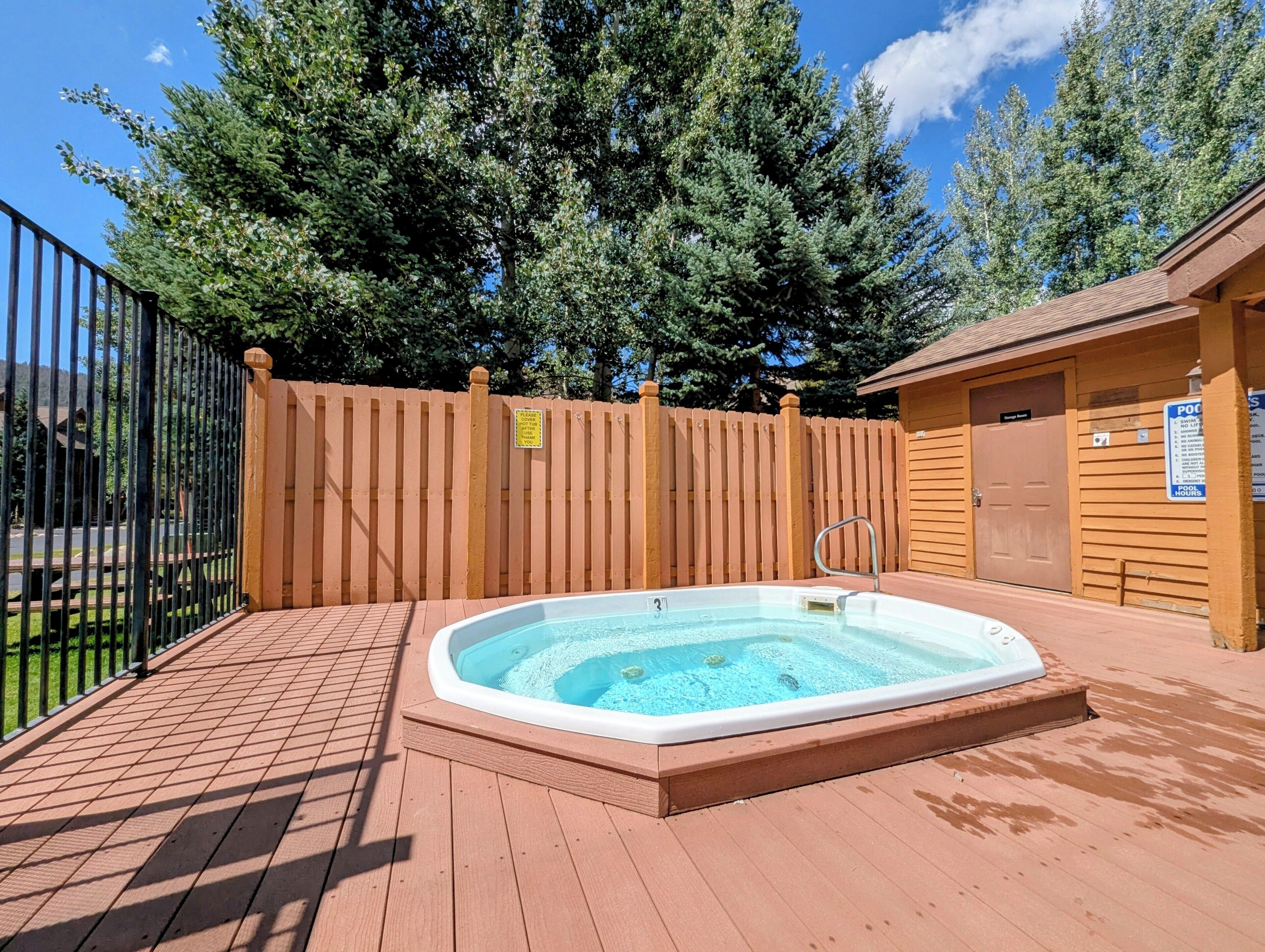 A hot tub on a wooden deck with a wooden fence and a pool house in the background.