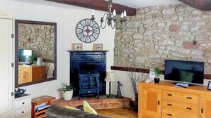 A living room with a stone wall, a fireplace, a large clock, a television, and a sofa. - 1 bedroom accommodation in Middleton-by-Wirksworth, near Wirksworth (Middleton-by-Wirksworth, near Wirksworth)