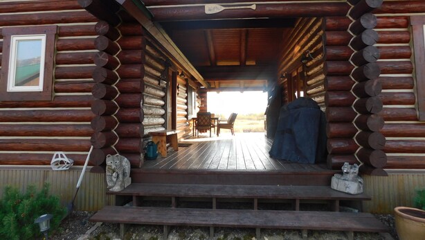 Eine Blockhütte mit einer Holzterrasse, einem überdachten Sitzbereich und Blick auf die umliegende Landschaft.