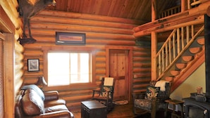 Ein Blockhaus-Interieur mit Ledersofa, Holzstuhl, Kamin und Treppe.