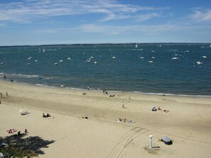 A beach with people sunbathing and swimming, boats on the water, and a clear sky.