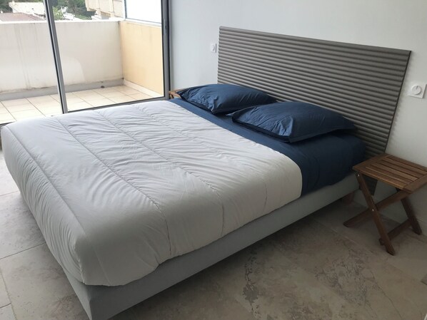 A bed with a grey headboard, a wooden nightstand, and a view of the outside through a sliding door.
