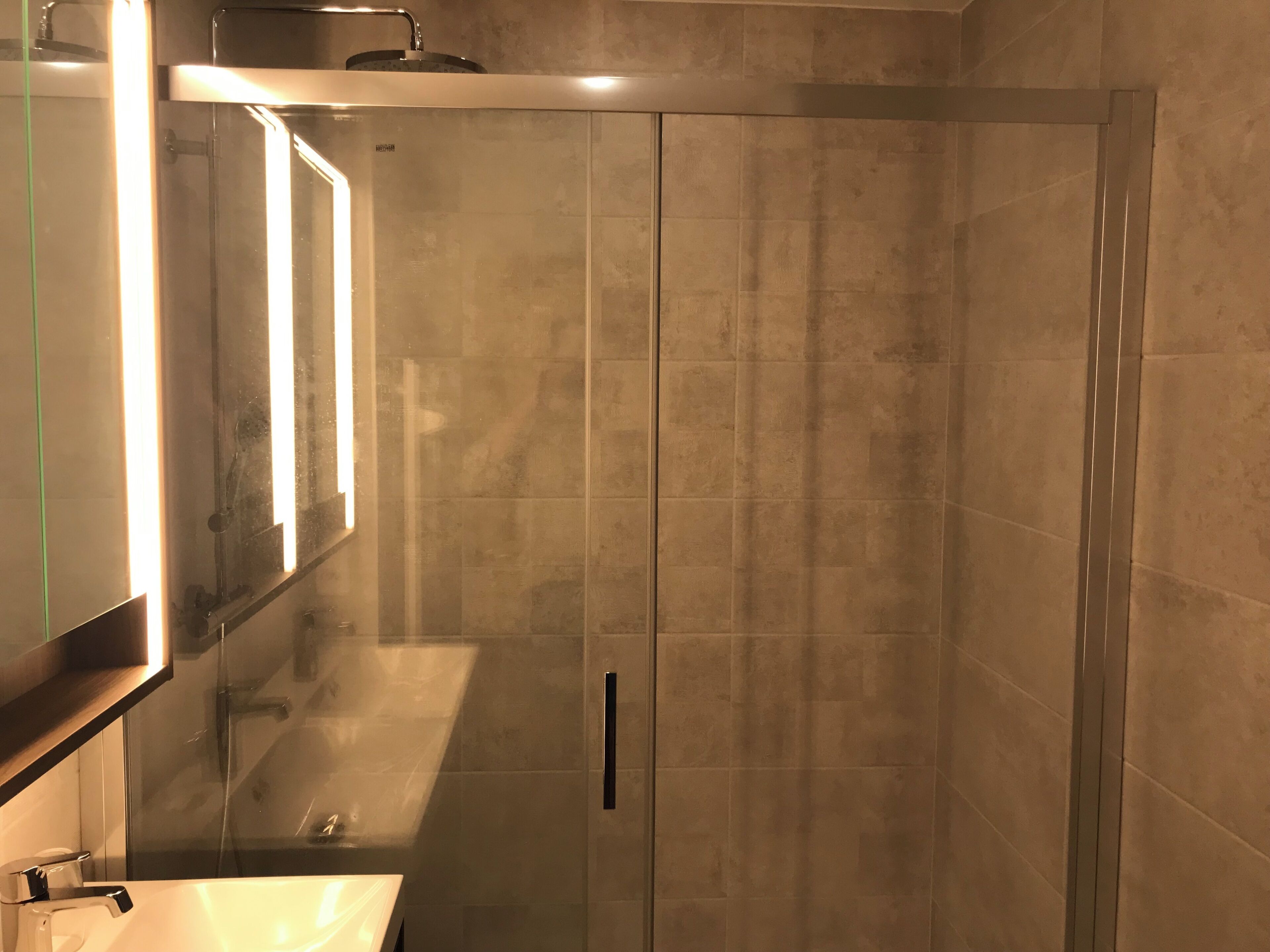 Une salle de bain moderne avec une douche à parois de verre, un lavabo avec un miroir et un porte-serviettes.