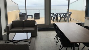 A balcony with a table and chairs, a sofa, and a view of the sea.