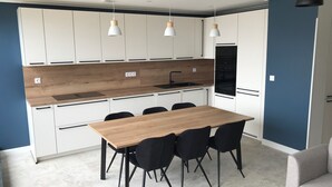 A modern kitchen with white cabinets, a wooden countertop, and black chairs around a wooden table.