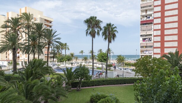 Een hotel met een zwembad, palmbomen en uitzicht op het strand.