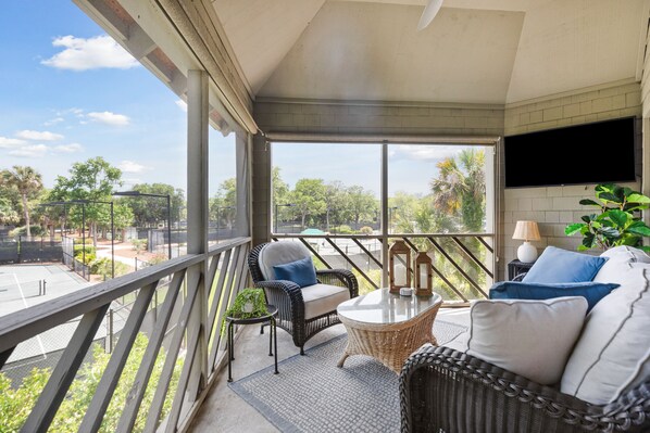A balcony with wicker furniture, a TV, and a view of the outdoors.