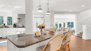 Una cocina amplia con una isla central, armarios blancos y un comedor con sillas de mimbre.