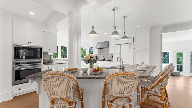 Una cocina amplia con muebles blancos, una isla central con taburetes de bar, electrodomésticos de acero inoxidable e iluminación colgante.