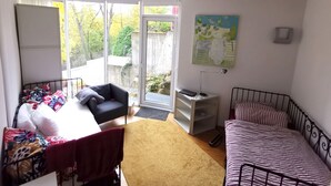 A small, well-lit room with a bed, a chair, a desk, and a window.