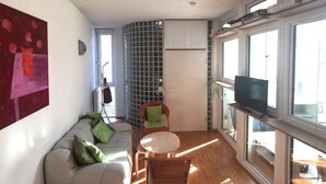 A modern living room with a sofa, a small round table, a television, and a large window.
