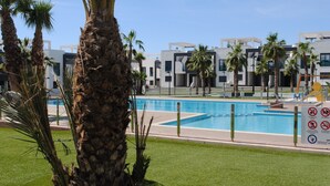 Ein modernes Hotel mit Schwimmbad, Palmen und blauem Himmel.