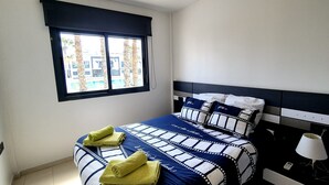 Ein Schlafzimmer mit einem Bett, einem Fenster, einem Nachttisch und einer Lampe.