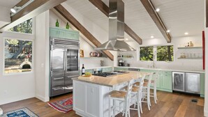 A modern kitchen with a central island, stainless steel appliances, and a rustic ceiling. - Pebble Beach's Empire (Pebble Beach)