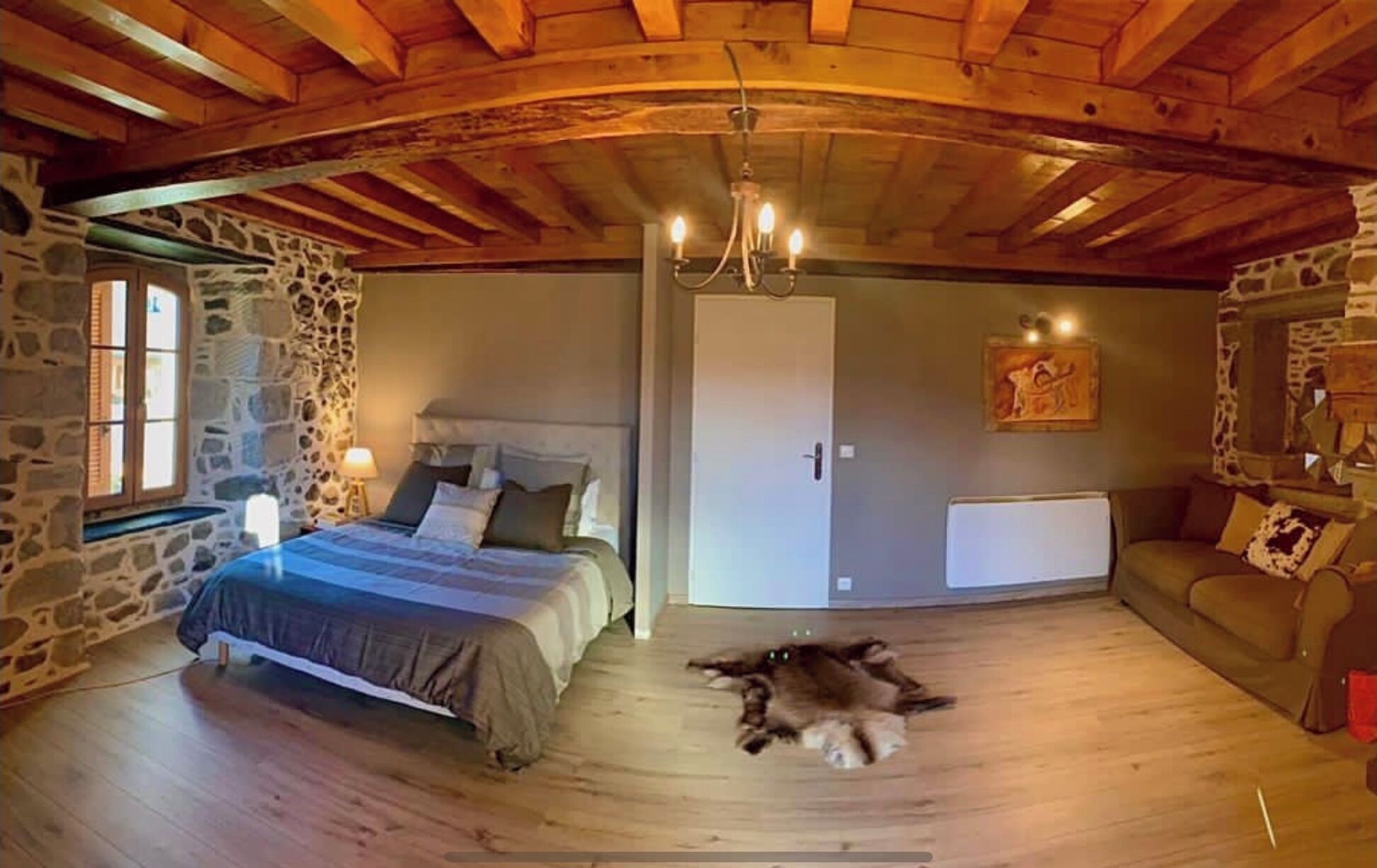 Un dormitorio acogedor con pared de piedra, techo de madera, una cama, un gato en el suelo y un sofá.