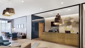 Un área de recepción moderna con un mostrador de madera, un espacio de espera con sofás y sillones, y decoración mural.