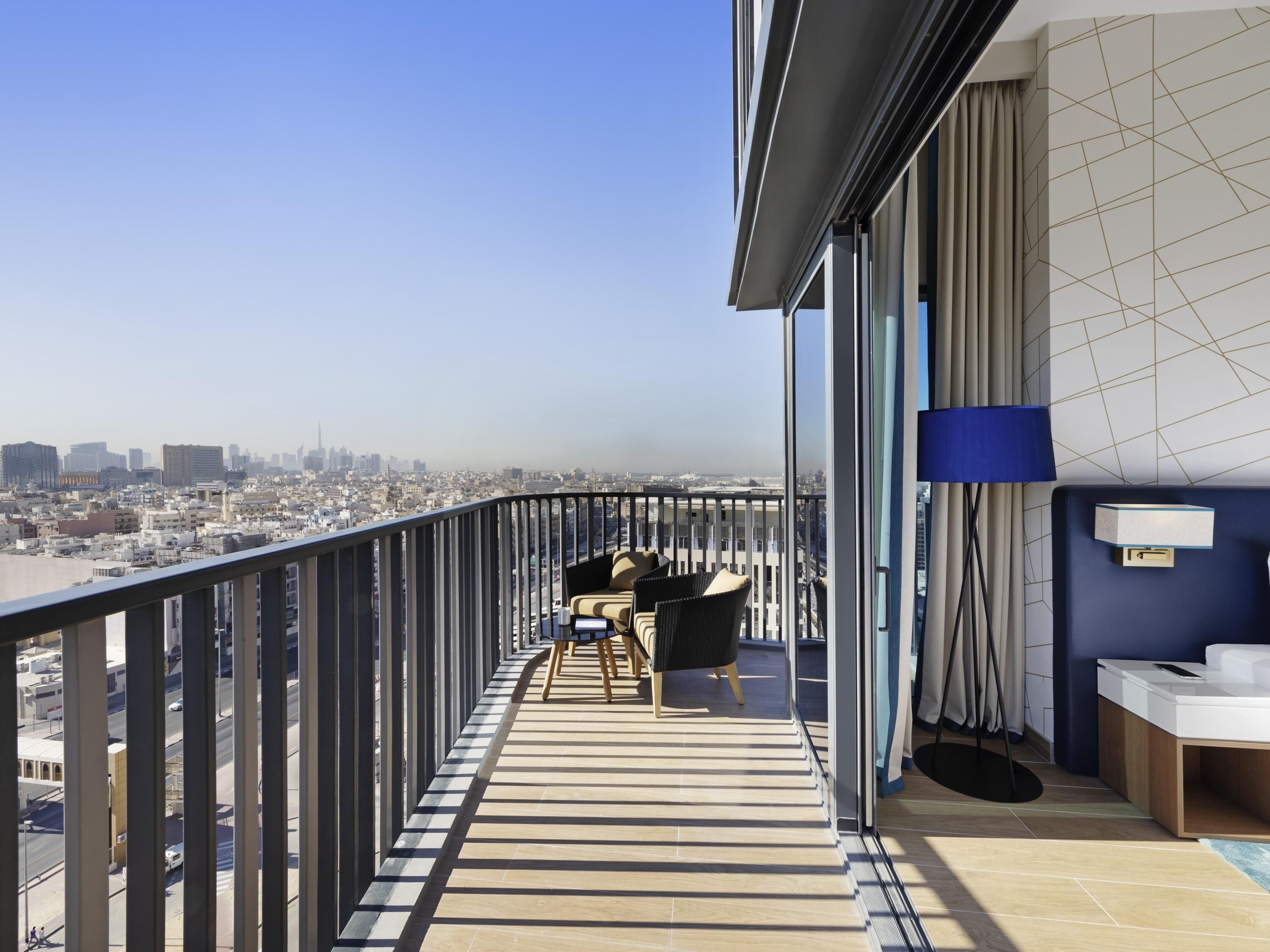Un balcón con vistas a la ciudad, una zona de comedor con sillas, una lámpara y una mesita.