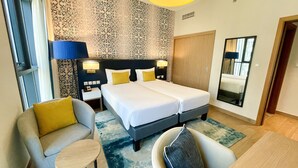 A hotel room with a double bed, two bedside tables with lamps, a sofa, a small round table, and a mirror. - Aparthotel Adagio Dubai Gold District (Dubai)