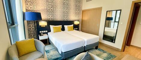 Ein Hotelzimmer mit Doppelbett, zwei Nachttischen mit Lampen, einem Sofa, einem kleinen runden Tisch und einem Spiegel.