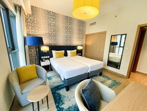 Habitación de hotel con cama doble, dos mesitas de noche con lámparas, un sofá, una mesa redonda pequeña y un espejo.