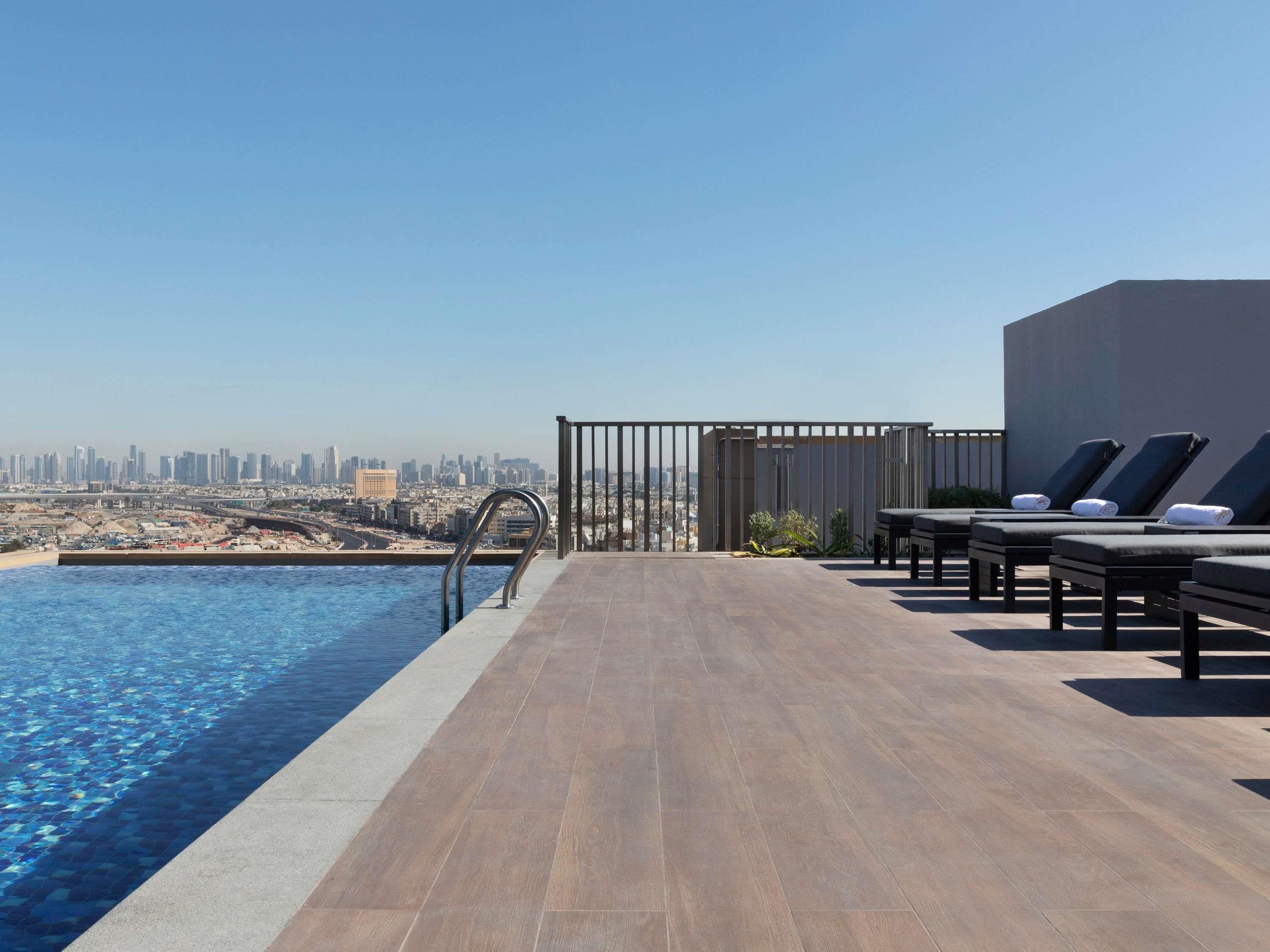 A rooftop pool area with a city view, lounge chairs, and a modern railing.