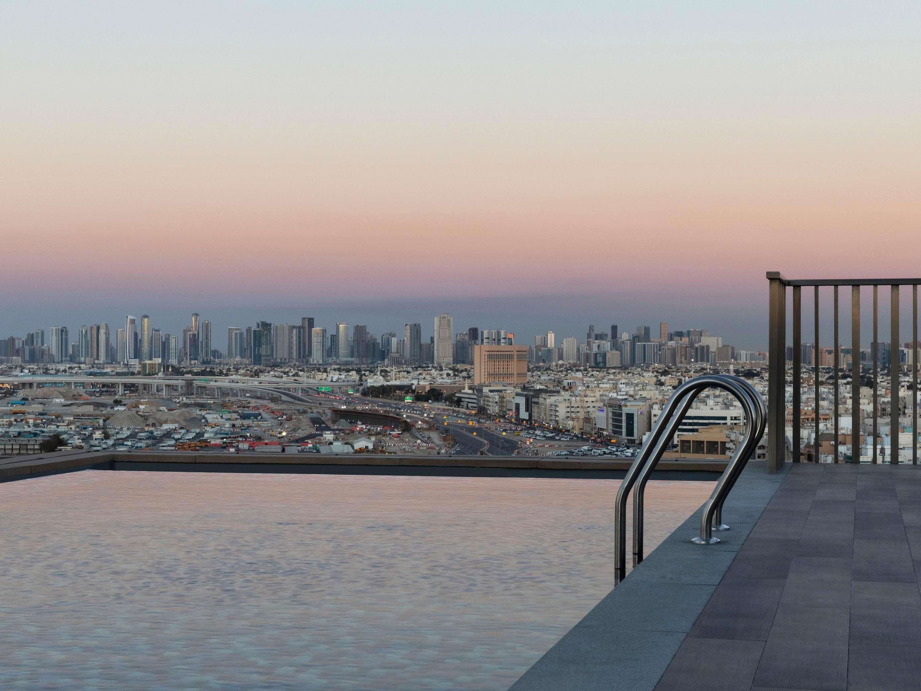 A cityscape view from a rooftop terrace with a swimming pool and a metal railing.