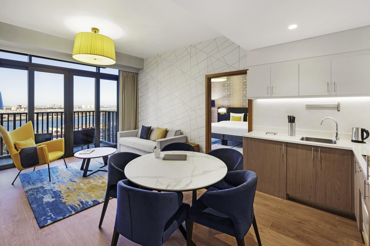 Una habitación de hotel moderna con balcón, una mesa de comedor redonda y una zona de cocina.
