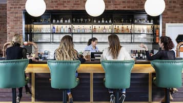 A bar area with a bartender, four bar stools, and a brick wall with shelves of bottles.