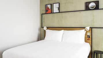 Una cama bien hecha con sábanas blancas en una habitación con pared de hormigón y cabecero de madera.