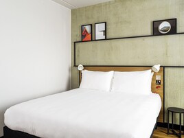 Uma cama bem arrumada com lençóis brancos em um quarto com parede de concreto e cabeceira de madeira.
