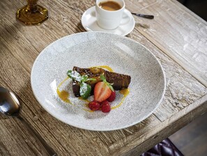 A dessert plate with chocolate cake, strawberries, and mint on a textured table.