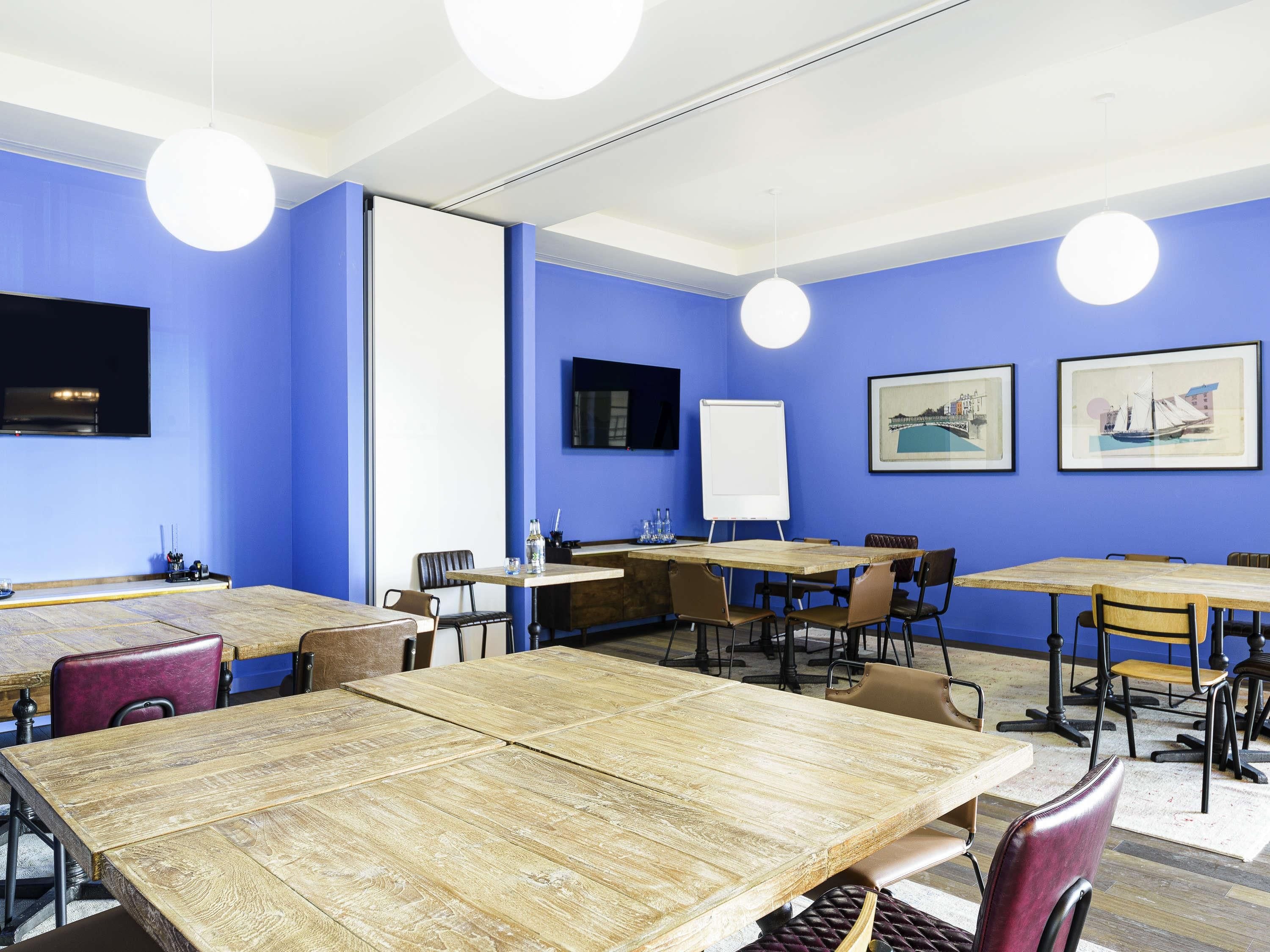 Ein Konferenzraum mit blauen Wänden, Holztischen und -stühlen, ausgestattet mit einer Whiteboard und einem Flachbildfernseher.