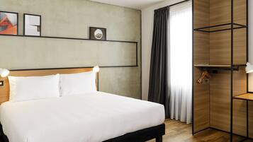 Habitación de hotel ordenada con una cama grande, un armario de madera y una estantería con fotografías.