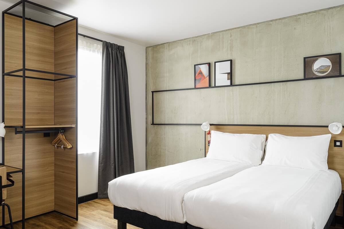 A hotel room with a bed, a wardrobe, a desk, and a window with curtains.