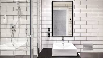 Un baño moderno con cabina de ducha de vidrio, un lavabo blanco con encimera negra y un espejo grande sobre el lavabo.