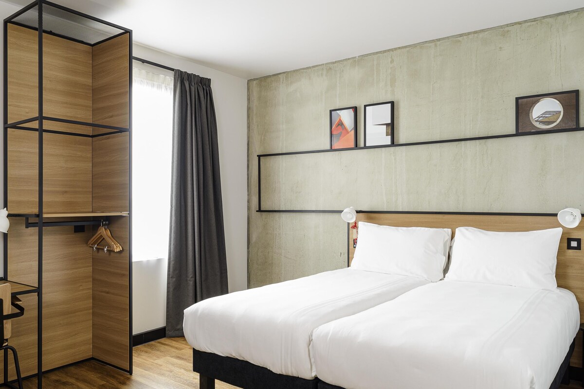 A hotel room with a bed, a wardrobe, a desk, and a window with curtains.