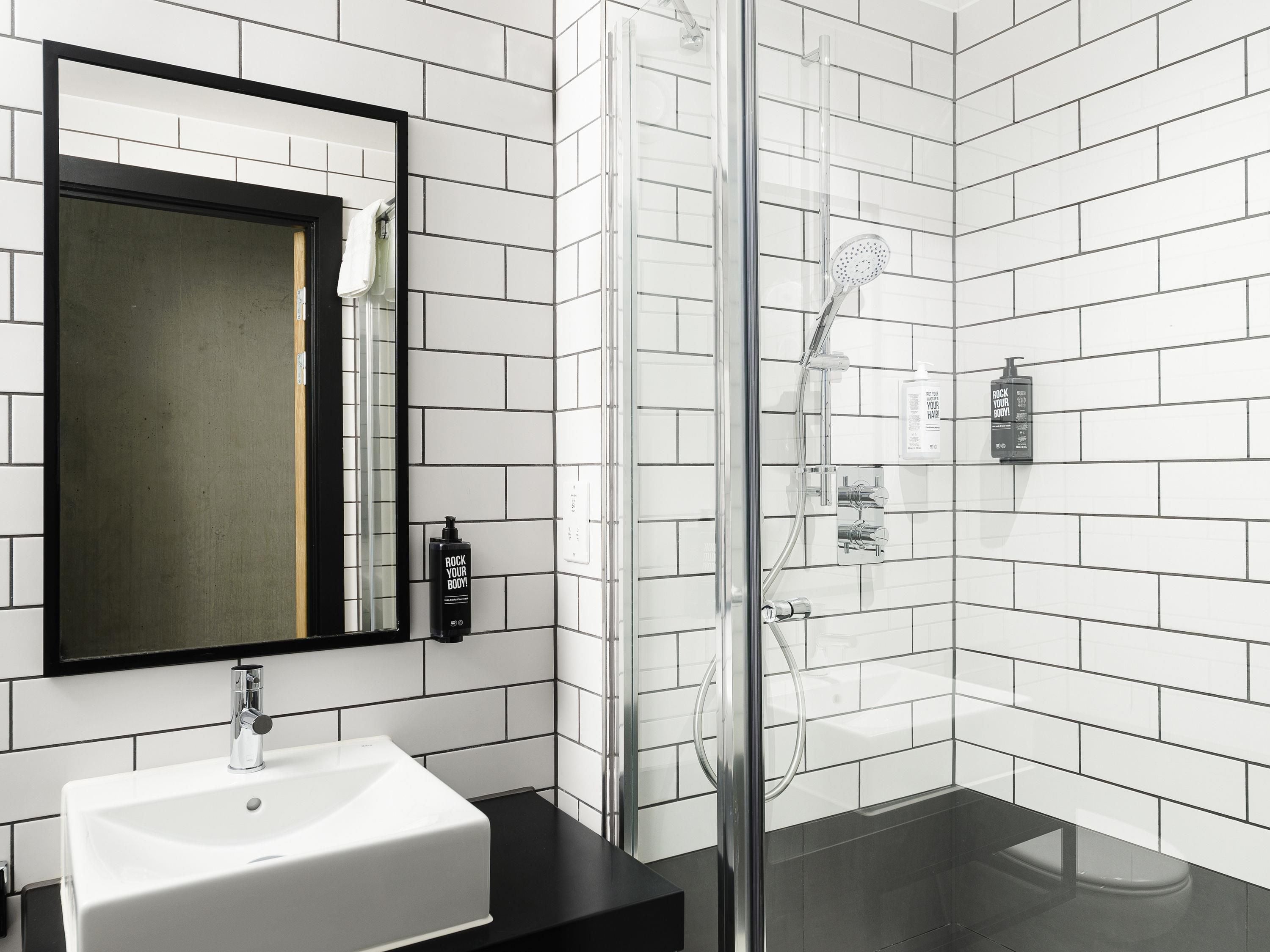 A modern bathroom with a white sink, a glass shower enclosure, and a black countertop.