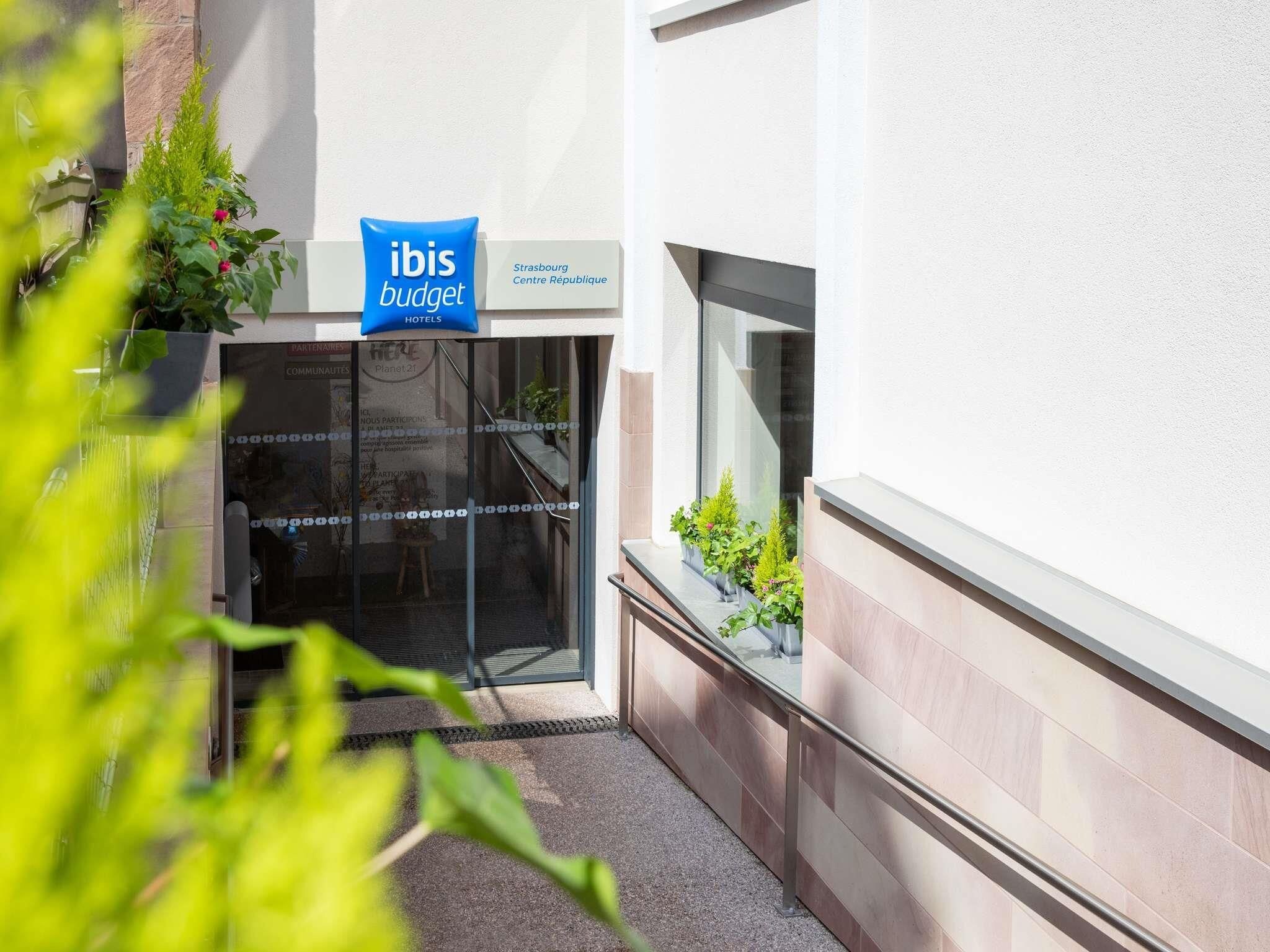 A building entrance with a sign for 'ibis budget hotels' and a window with plants.