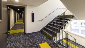 Un couloir d’hôtel avec un escalier, un panneau d’identification des numéros de chambre et une moquette à motifs.