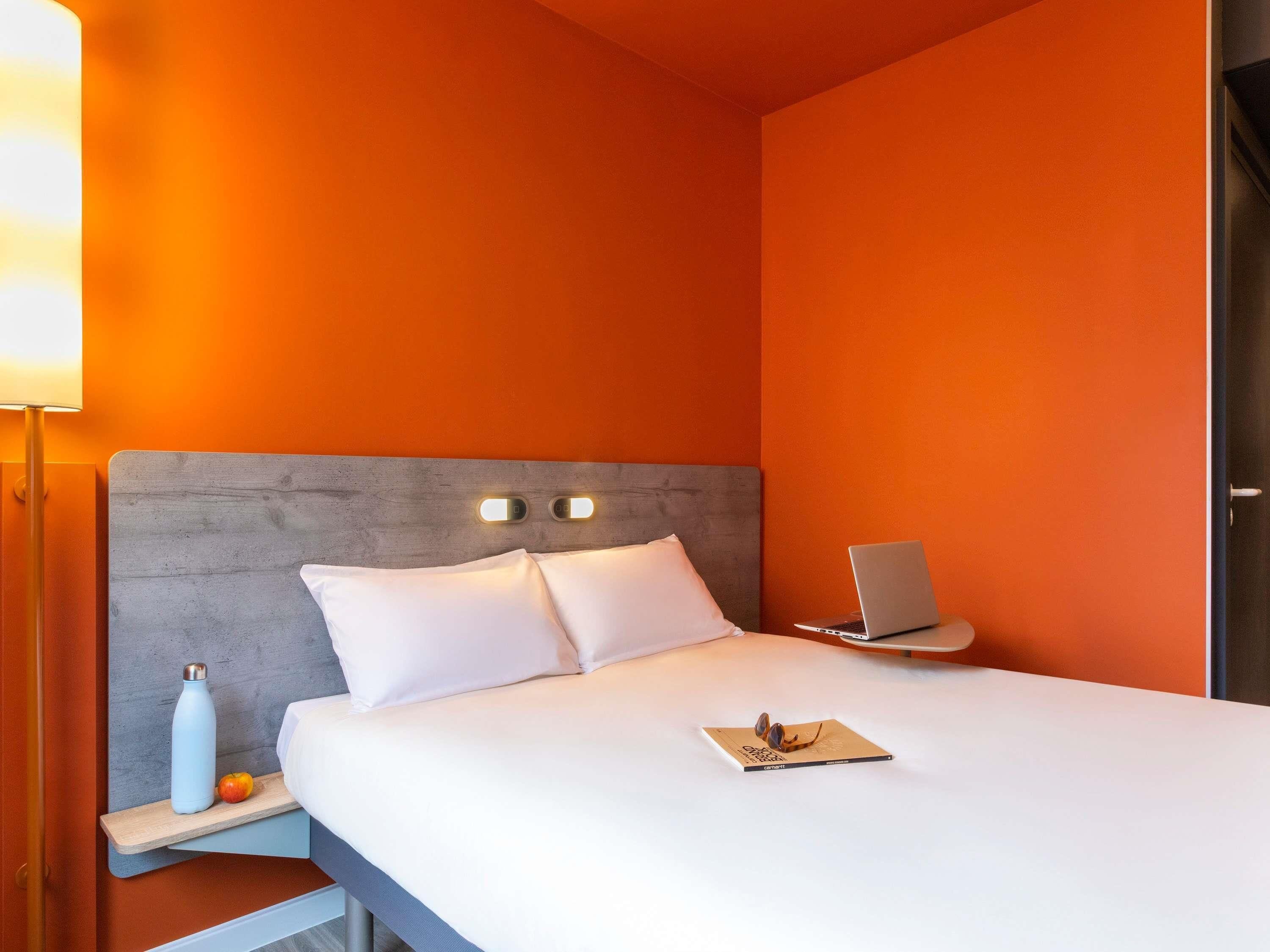 Een hotelkamer met een bed, nachtkastje met lamp, een laptop en een boek.