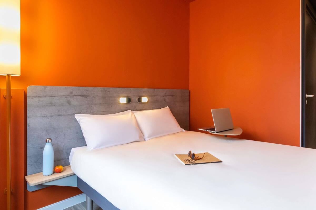 Een hotelkamer met een bed, nachtkastje met lamp, een laptop en een boek.