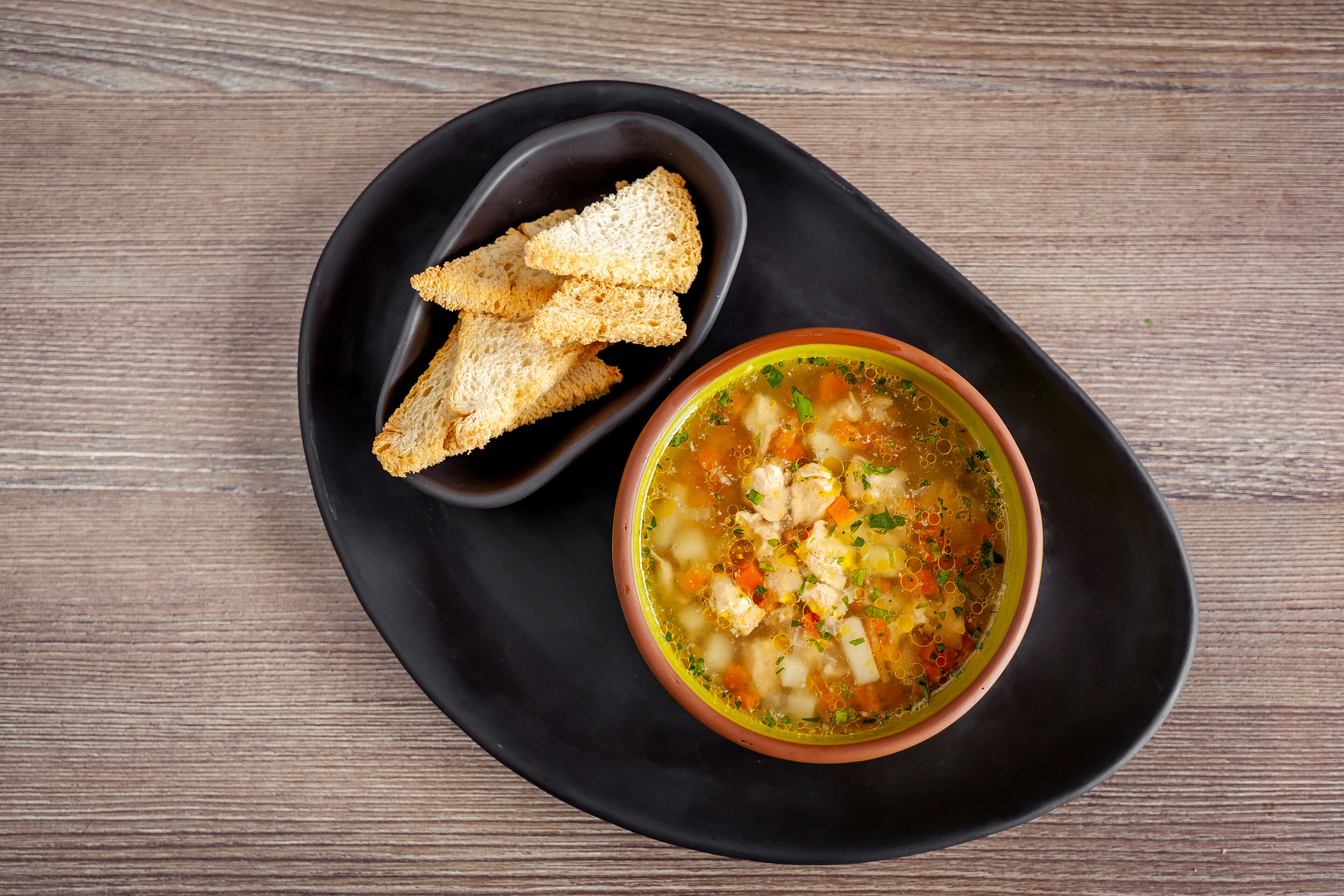 A bowl of soup with croutons on a black plate.