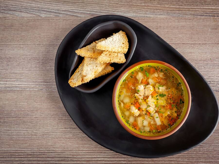 A bowl of soup with croutons on a black plate.