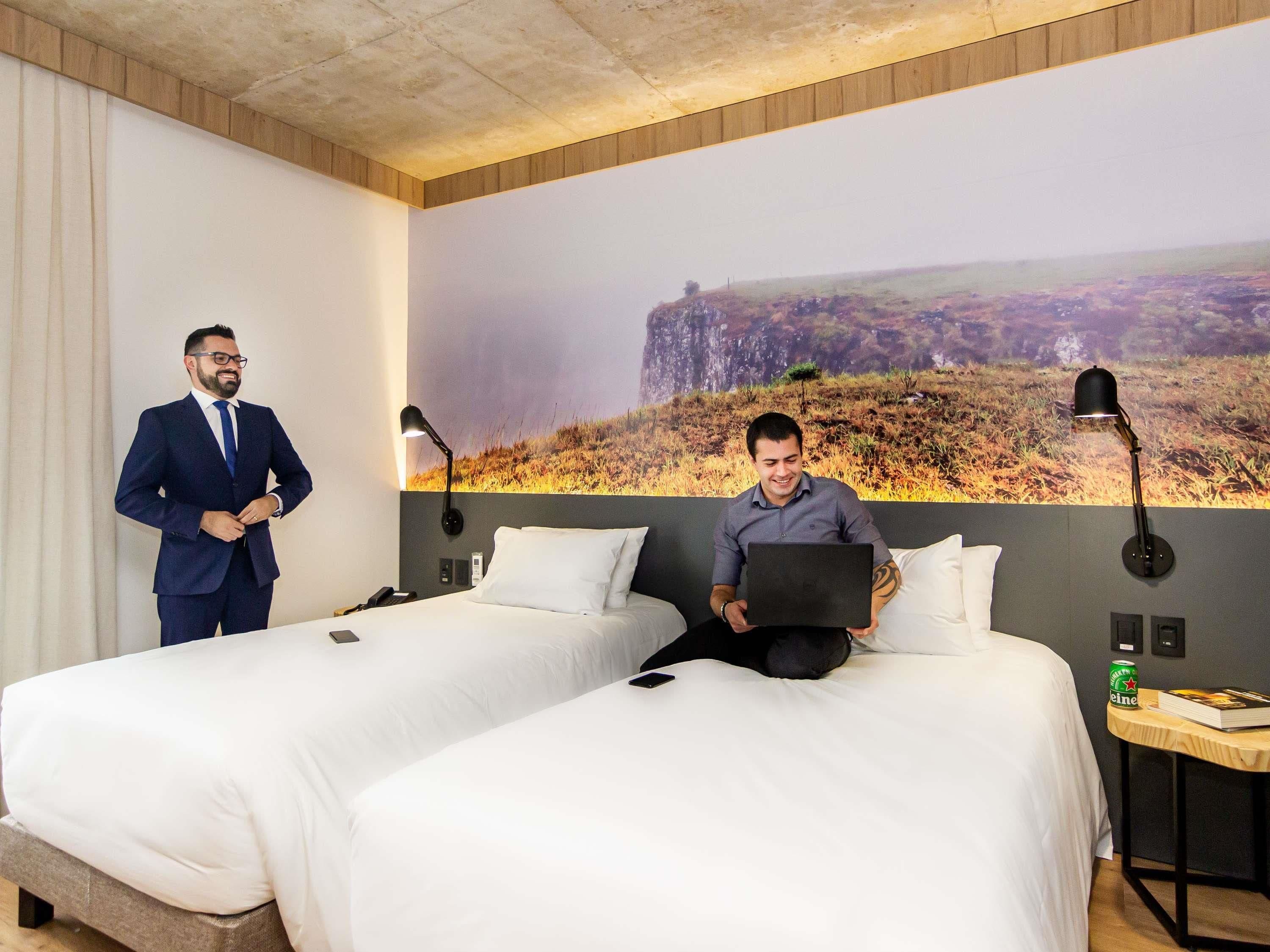 Een hotelkamer met twee bedden, een groot muurschildering en een kleine tafel met een lamp.