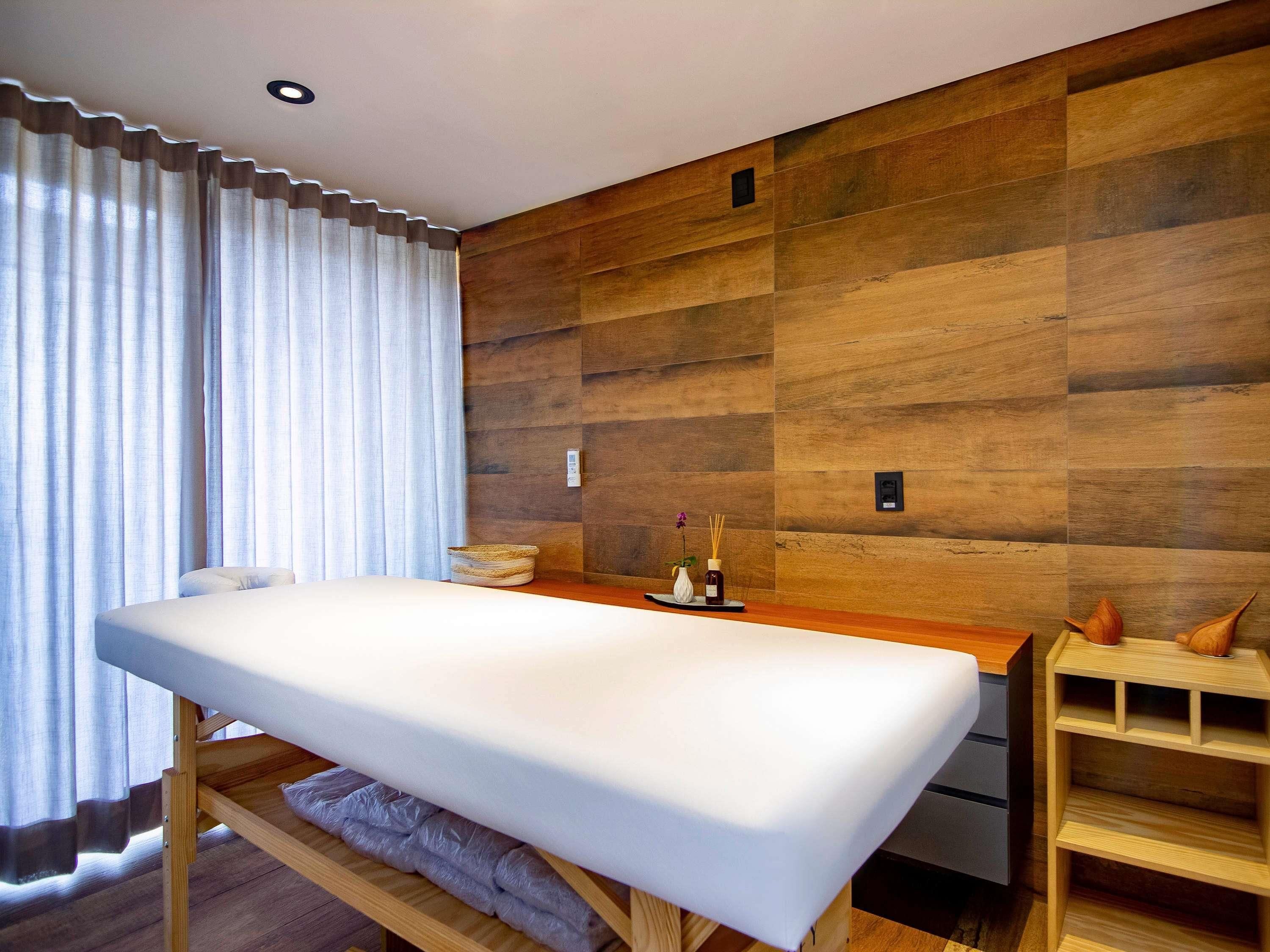 Quarto moderno com parede de madeira, uma cama, uma pequena mesa de madeira e uma janela com cortinas.