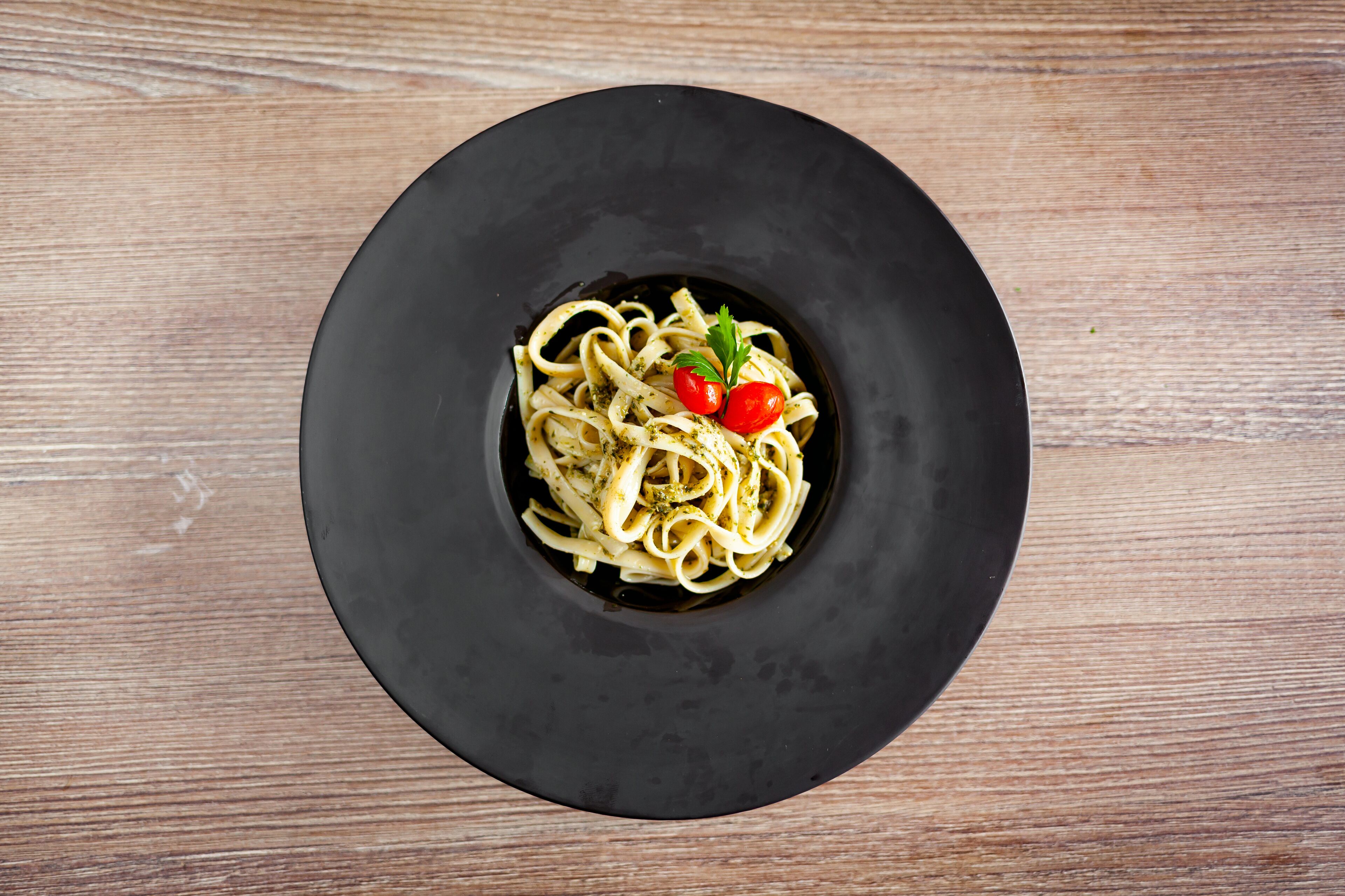A black plate with pasta and cherry tomatoes on a wooden table.