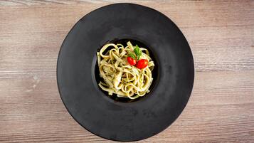 A black plate with pasta and cherry tomatoes on a wooden table.