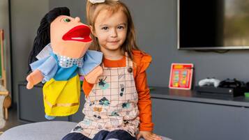 Un niño sentado en un taburete gris con un títere a su lado.