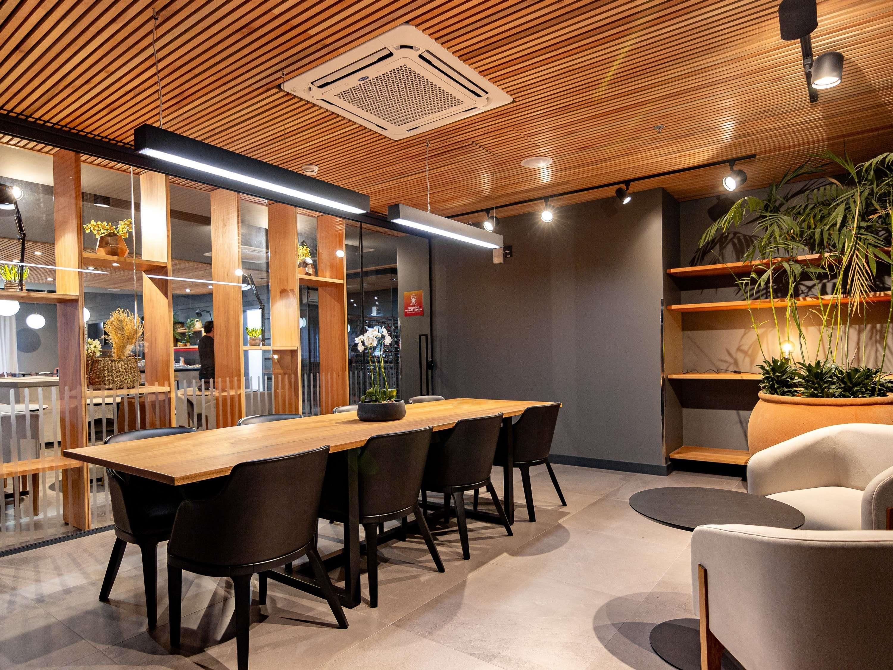 Un interior moderno con techo de madera, una mesa larga con sillas y plantas en macetas.