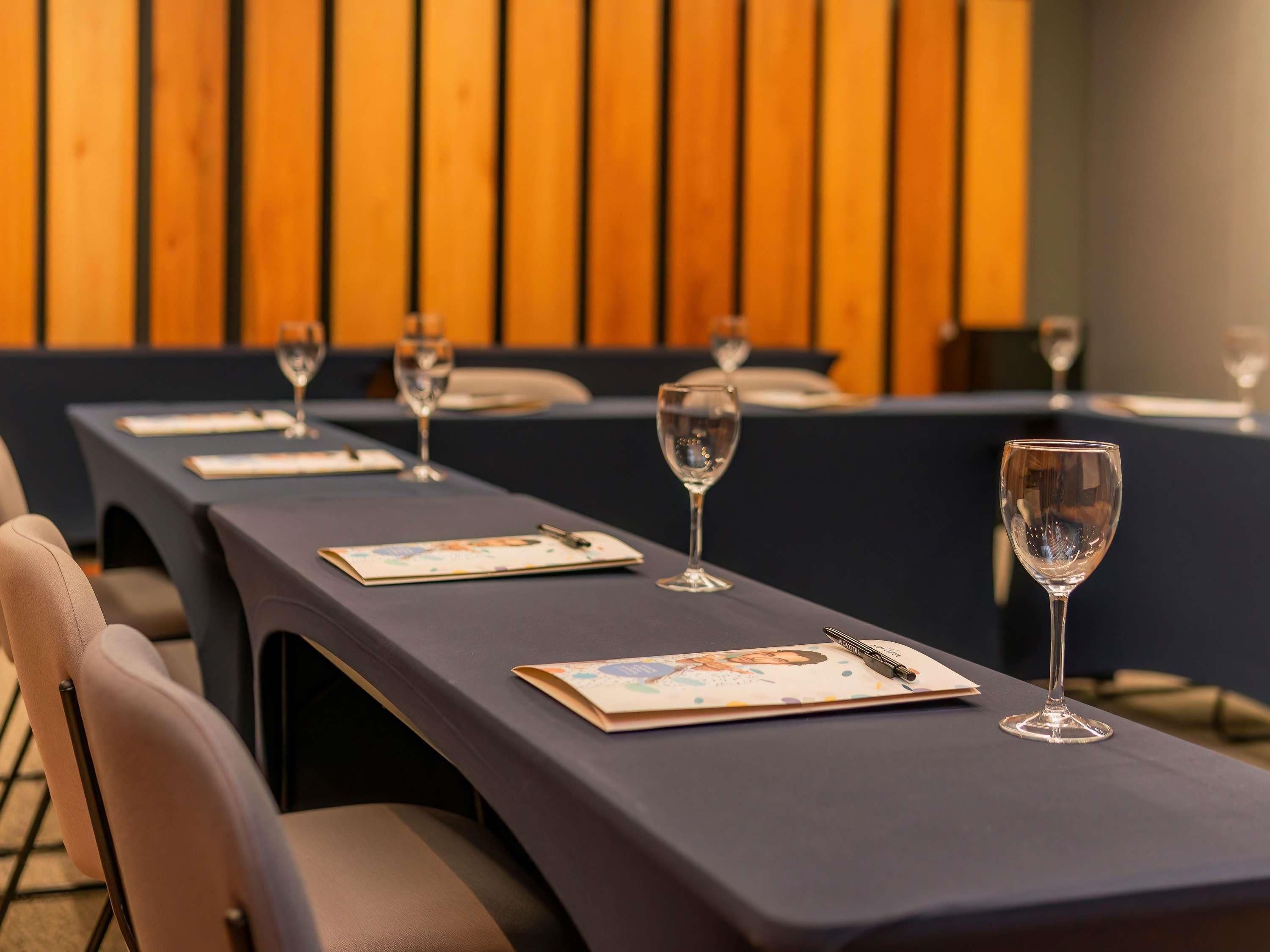 Un salón de conferencias con largas mesas, sillas y copas de vino vacías.